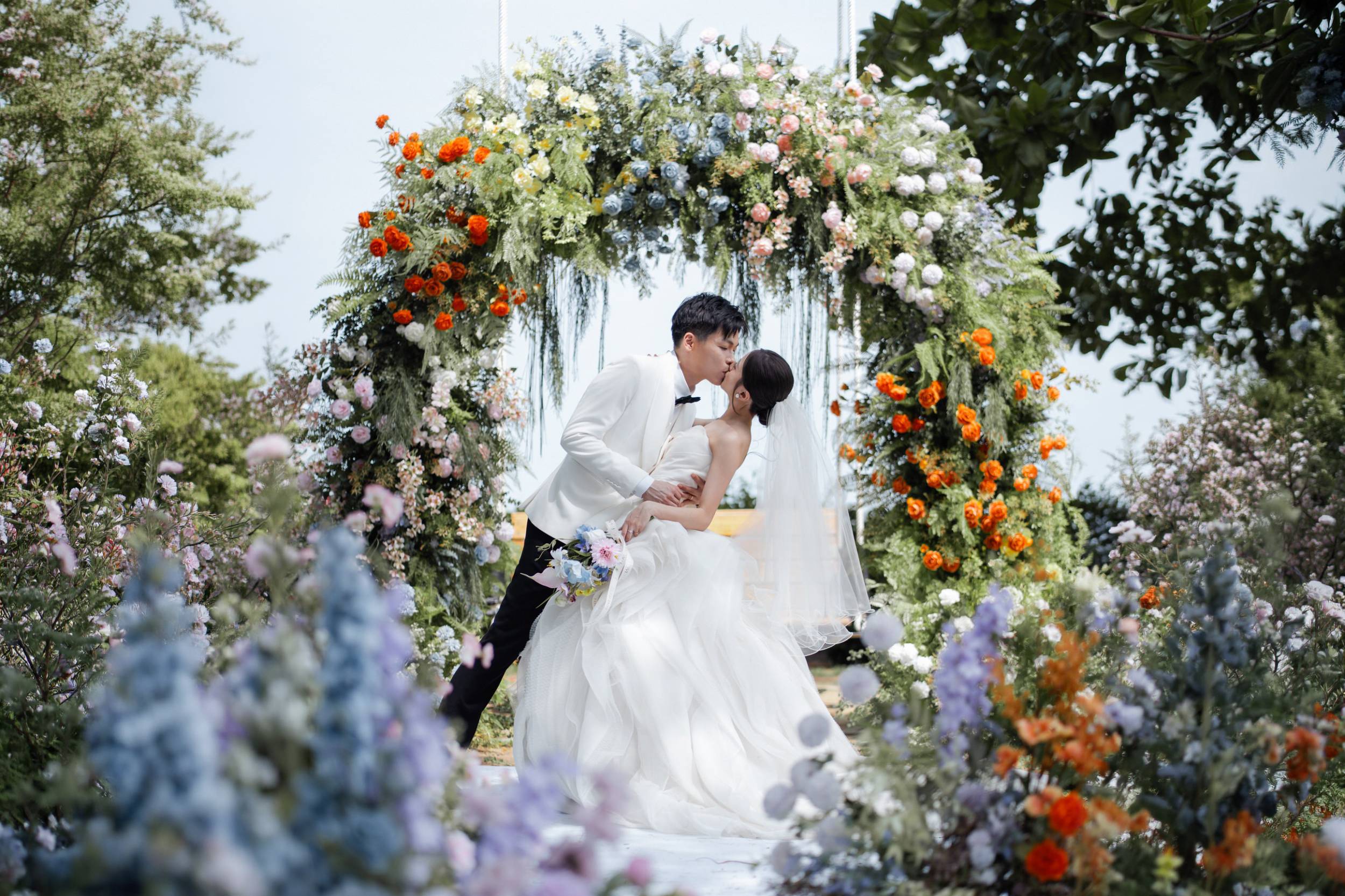 Bride and groom kissing beneath floral swing arch at Parkroyal Penang garden wedding