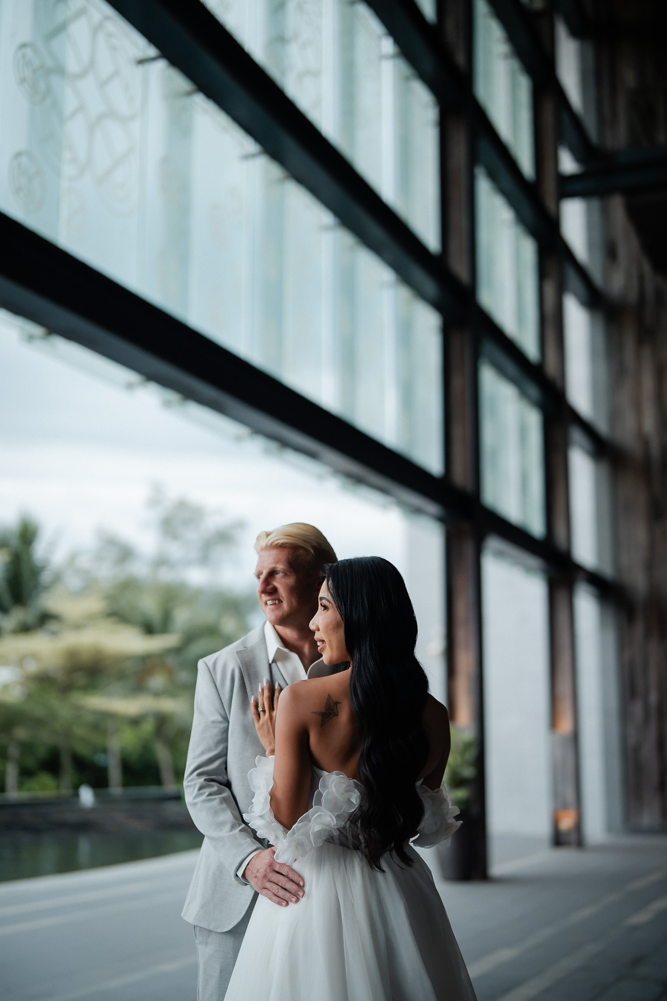 Angsana Beach Resort Penang bride and groom embrace under modern glass pavilion, gazing into tropical greenery.