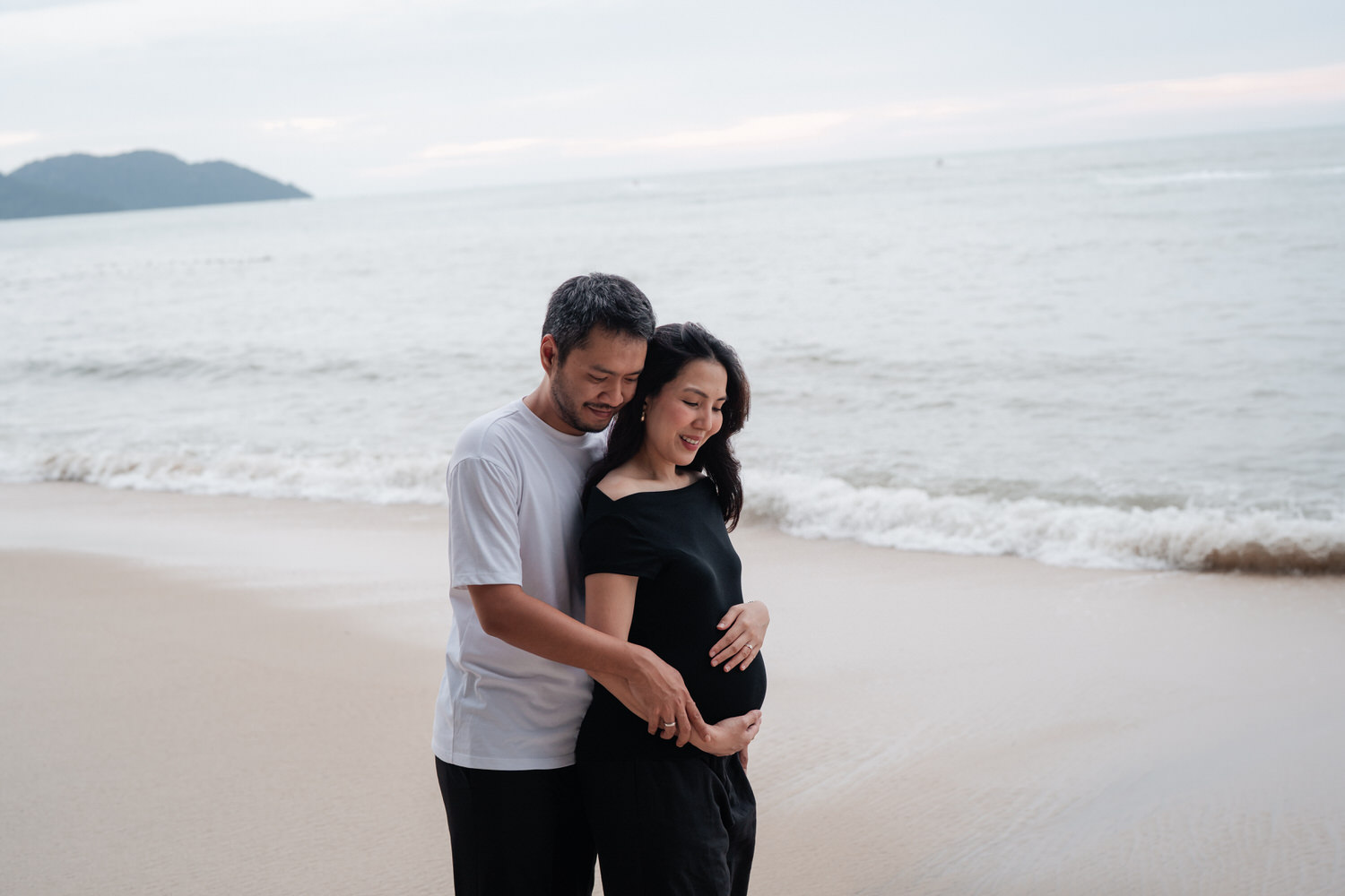 Joyful maternity couple smiling together on the curved concrete walkway along winding garden path with Lone Pine Hotel gro...