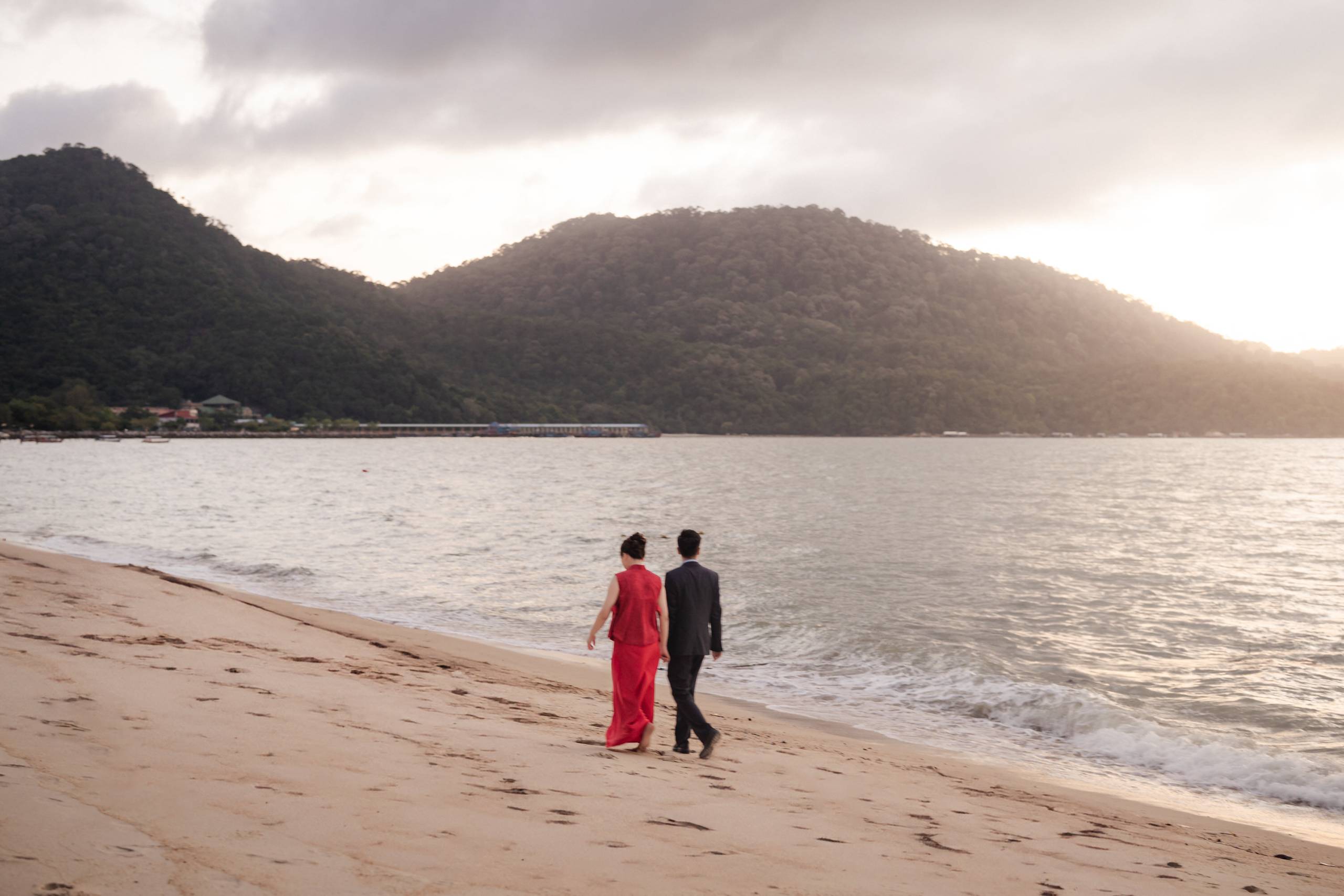 Couple walking along the beach at Angsana Teluk Bahang with sunset light over the water